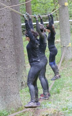 STOCKHOLM, SWEDEN - MAY 14, 2016: Side view of three woman with mud in their face trying to maintain the balance on a slack rope in the obstacle race Tough Viking Event in Sweden, April 14, 2016