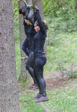 STOCKHOLM, SWEDEN - MAY 14, 2016: Side view of three woman with mud in their face trying to maintain the balance on a slack rope in the obstacle race Tough Viking Event in Sweden, April 14, 2016