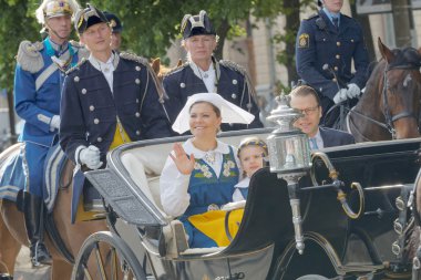 STOCKHOLM, SWEDEN - JUN 06, 2016: The swedish crown princess Victoria, prince Daniel and princess Estelle Bernadotte smiling and waiving to the audience from the royal coach on their way to celebrate the swedish national day. clipart