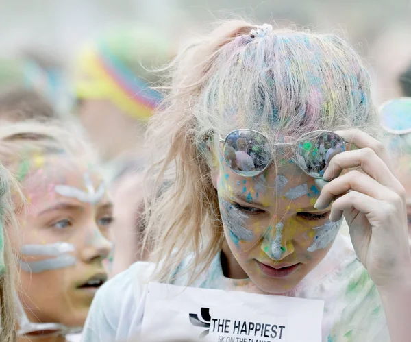 Girl covered with color powder wearing sun glasses in a crowd of — Stock Photo, Image