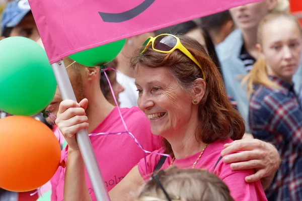 Mujer sonriente mayor sosteniendo una bandera de arco iris, fondo colorido — Foto de Stock