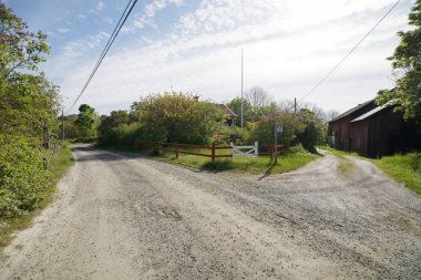 Baharda küçük köyün kırsal kesiminde çatal, uzak kırmızı kulübe ve ahır, mavi gökyüzü ve ağaçlar