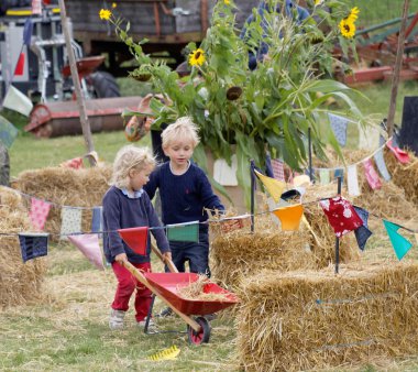 Children playing with hay and a wheel barrow
