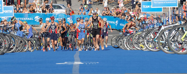 STOCKHOLM, SWEDEN - AUG 23, 2015: Chaotic scene with running triathletes with bicycles in the transition zone, bus and sea in the background in the Men's ITU World Triathlon series event August 23, 2015 in Stockholm, Sweden