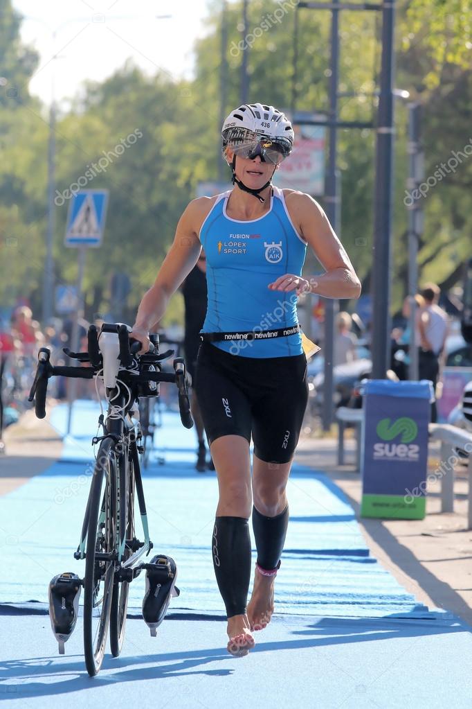 Woman running barefoot with bicycle in the triathlon transition