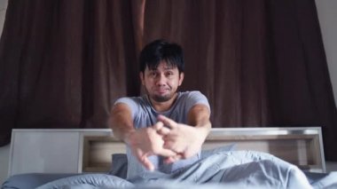 Asyalı bir adam sabah uyandıktan sonra yatağa uzanıyor.