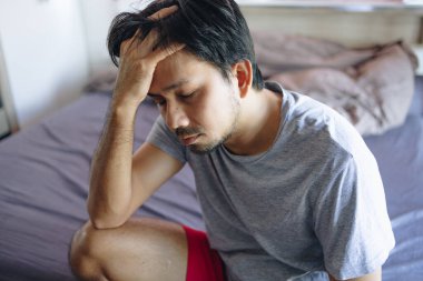 Asian man suffering from stress or a headache in the bedroom