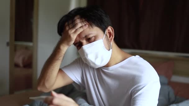 亚洲病人戴着面部防护面具 在家里卧室里看温度计发高烧 — 图库视频影像