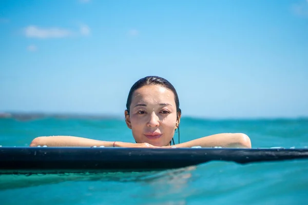 Portrait of surfer girl on surf board in blue ocean pictured from the water in Bali