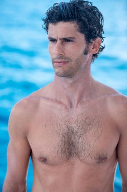 Yakışıklı bir adamın portresi, gömleksiz bir sörfçü ve arkasında mavi bir okyanus.