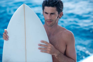 Yakışıklı bir adamın portresi, üstsüz sörfçü yatta açık havada duş alıyor ve mavi okyanus arka planda.