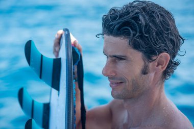 Yakışıklı bir adamın portresi, üstsüz sörfçü yatta açık havada duş alıyor ve mavi okyanus arka planda.