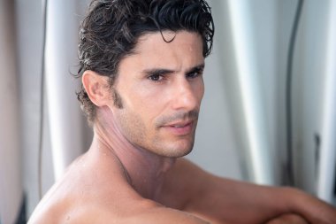 Yakışıklı bir adam portresi, beyaz dişli üstsüz sörfçü gülüşü ve arka planda mavi okyanus.