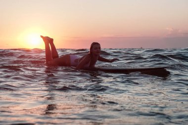 Bali 'de gün batımında okyanusta sörf tahtasında güzel vücutlu sörfçü kızın sularından bir portre.