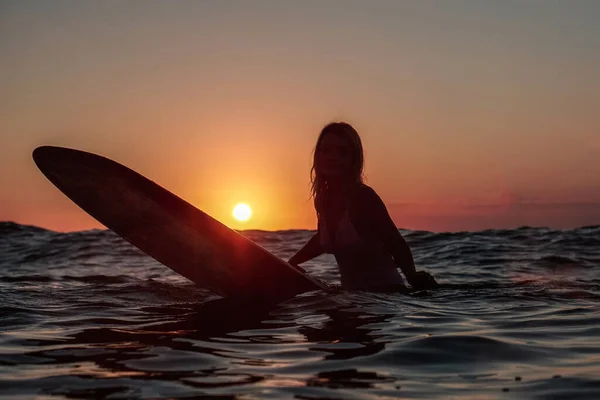 バリの日没時に海のサーフボードに美しい体を持つサーファーの女の子の水からの肖像画 — ストック写真