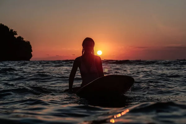 バリの日没時に海のサーフボードに美しい体を持つサーファーの女の子の水からの肖像画 — ストック写真