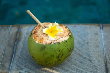 Yeşil genç hindistan cevizi, Bali 'de yüzme havuzunun kenarında bambu kamışı ve tropikal çiçek frangipani ile yakınlaşır.