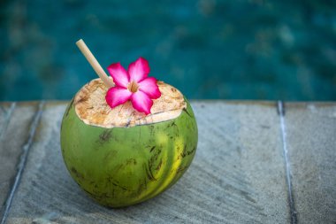 Yeşil hindistan cevizi, Bali 'de yüzme havuzunun kenarında bambu kamışı ve tropikal pembe çiçekle yakın plan.