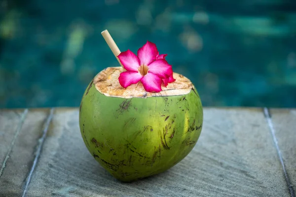 バリ島のプールの端にある竹の藁と熱帯ピンクの花で閉じられた緑の若いココナッツ — ストック写真
