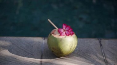 Yeşil genç hindistan cevizi görüntüsü Bali 'de yüzme havuzunun kenarında bambu kamışı ve tropikal pembe çiçekle yakınlaşıyor.