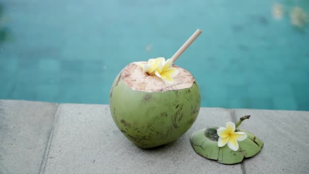 バリ島のスイミングプールの端にある竹の藁と熱帯の花Frangipaniで閉じられた緑の若いココナッツの映像 — ストック動画