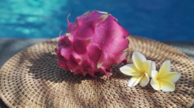 Video görüntüleri, taze kırmızı ejderha meyvesiyle yüzme havuzunun kenarında beyaz tropikal çiçeklerle frangipani 'yi, palmiye dalından gölgeyi ve Bali' de arka planda kaynayan mavi havuz suyunu gösteriyor. 