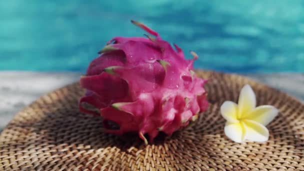 在巴厘岛拍摄的视频镜头中 新鲜的红色龙果在游泳池边滴入清澈的水珠 白色热带花 从棕榈枝移出阴影 水泡蓝色水泡在背景下 — 图库视频影像