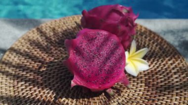 Taze kırmızı ejderha meyvesi, köpüren mavi yüzme havuzunun kenarında taze hamurla ikiye bölünmüş beyaz tropikal çiçekler frangipani,