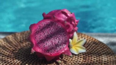 Taze kırmızı ejderha meyvesi, köpüren mavi yüzme havuzunun kenarında taze hamurla ikiye bölünmüş beyaz tropikal çiçekler frangipani,