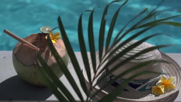 竹の藁 太陽の帽子 熱帯の黄色の花Frangipani バリ島のスイミングプールの端にあるヤシの木陰で閉じられる緑の若いココナッツのビデオ — ストック動画