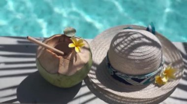 Yeşil hindistancevizinin video görüntüleri bambu kamışı, güneş şapkası, tropik sarı çiçek frangipani, Bali 'de yüzme havuzunun kenarında palmiye gölgesi
