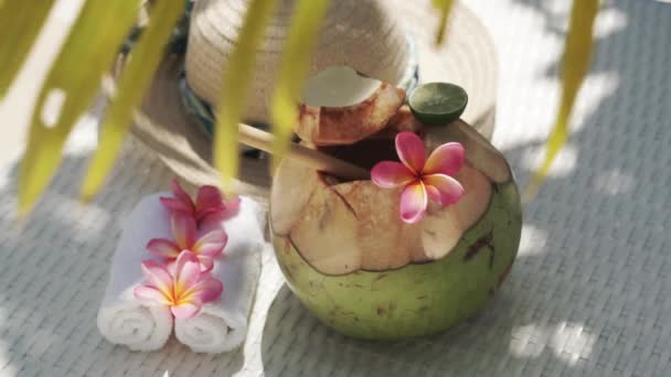 緑の若いココナッツのビデオ映像は 竹の藁 太陽の帽子 熱帯の花Frangipani バリ島の白い太陽のベッドの上のヤシの木陰で閉じます — ストック動画