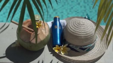 Yeşil hindistancevizinin video görüntüleri bambu kamışı, bir şişe güneş kremi 50, güneş şapkası, tropik sarı çiçek frangipani, Bali 'de yüzme havuzunun kenarında palmiye gölgesi