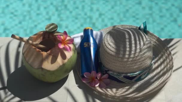 竹の藁で閉じ緑の若いココナッツのビデオ映像 日焼け止めのボトルSpf 太陽の帽子 熱帯ピンクの花Frangipani バリ島のスイミングプールの端にヤシの木陰 — ストック動画