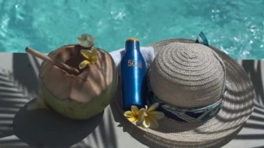 Yeşil hindistancevizinin video görüntüleri bambu kamışı, bir şişe güneş kremi 50, güneş şapkası, tropik sarı çiçek frangipani, Bali 'de yüzme havuzunun kenarında palmiye gölgesi