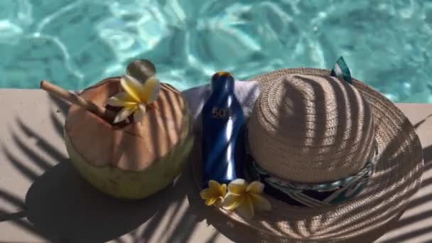 竹の藁で閉じ緑の若いココナッツのビデオ映像 日焼け止めのボトルSpf 太陽の帽子 熱帯黄色の花Frangipani バリ島のスイミングプールの端にヤシの木陰 — ストック動画