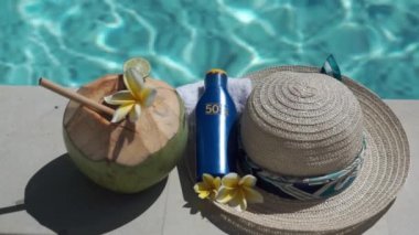 Yeşil hindistancevizinin video görüntüleri bambu kamışı, bir şişe güneş kremi 50, güneş şapkası, tropik sarı çiçek frangipani, Bali 'de yüzme havuzunun kenarında palmiye gölgesi