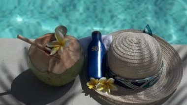Yeşil hindistancevizinin video görüntüleri bambu kamışı, bir şişe güneş kremi 50, güneş şapkası, tropik sarı çiçek frangipani, Bali 'de yüzme havuzunun kenarında palmiye gölgesi