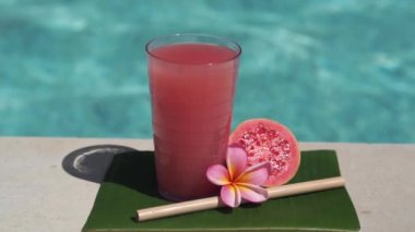Pembe guava suyu, bambu kamışı, taze pembe guava, tropikal çiçek frangipani ve arka planda kaynayan mavi yüzme havuzunun video görüntüleri..