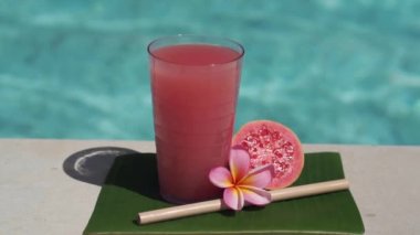 Pembe guava suyu, bambu kamışı, taze pembe guava, tropikal çiçek frangipani ve arka planda kaynayan mavi yüzme havuzunun video görüntüleri..
