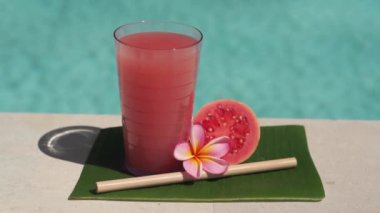 Pembe guava suyu, bambu kamışı, taze pembe guava, tropikal çiçek frangipani ve arka planda kaynayan mavi yüzme havuzunun video görüntüleri..