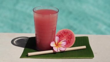Pembe guava suyu, bambu kamışı, taze pembe guava, tropikal çiçek frangipani ve arka planda kaynayan mavi yüzme havuzunun video görüntüleri..
