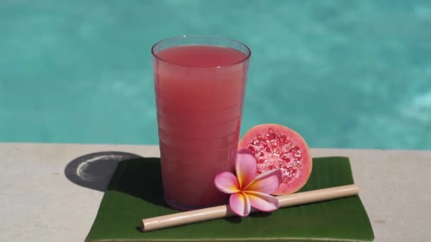 有粉色番石榴汁 一半新鲜的粉色番石榴 热带花 泡沫蓝色游泳池背景的玻璃杯录像带 — 图库视频影像