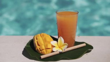 Mango suyu, bambu kamışı, taze mango, sarı frangipani çiçeği ve arka planda kaynayan mavi yüzme havuzunun video görüntüleri..