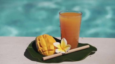 Mango suyu, bambu kamışı, taze mango, sarı frangipani çiçeği ve arka planda kaynayan mavi yüzme havuzunun video görüntüleri..