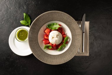 Taze domates ve fesleğen salatalı Mozzarella peyniri. Pesto sosuyla servis edilmiş. Restoran menüsü için sebze tabağı siyah taş bir masada çatal bıçakla servis edilir..