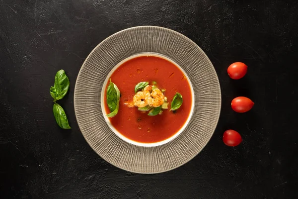 Klasik İspanyol domates çorbası karides, fesleğen yaprağı ve kiraz domatesli gazpacho siyah taş mutfak masasında..