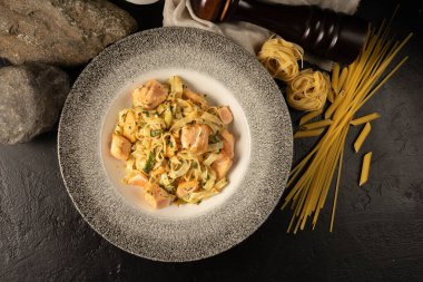 Uçan balık yumurtası ve soğandan somon ve balık soslu bir tabak pişmiş tagliatelle. Farklı çeşitlerdeki makarna masanın üzerinde hazır yemeğin yanında..