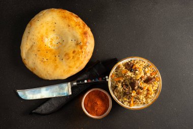 Pilaf, kuzu eti, sebze, baharat ve sıcak buğday ekmeğiyle birlikte geleneksel bir pirinç yemeğidir. Geleneksel Özbek desenli mutfak bıçağı..