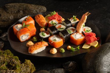 Güzel siyah bir tabakta bir suşi seti. Japon yemeği. Chuka salatası ve somonlu suşi, krem peynirli Philadelphia maki, sashimi, karides, zencefil, wasabi ve fıstık soslu makarna..